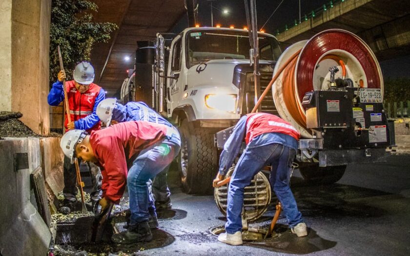 Street workers cleaning drainage at night with machinery under a bridge. - Photo by JESUS ADRIÁN SAAVEDRA on Pexels