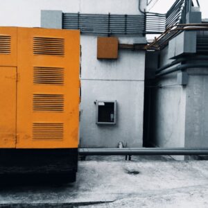 Outdoor view of an industrial generator with visible piping and wiring against a concrete wall. - Photo by ezrah lane on Pexels