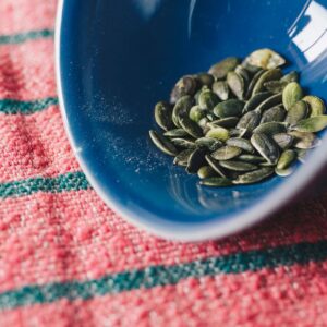 Close-up of pumpkin seeds in a blue bowl on a red patterned cloth. - Photo by João Jesus on Pexels