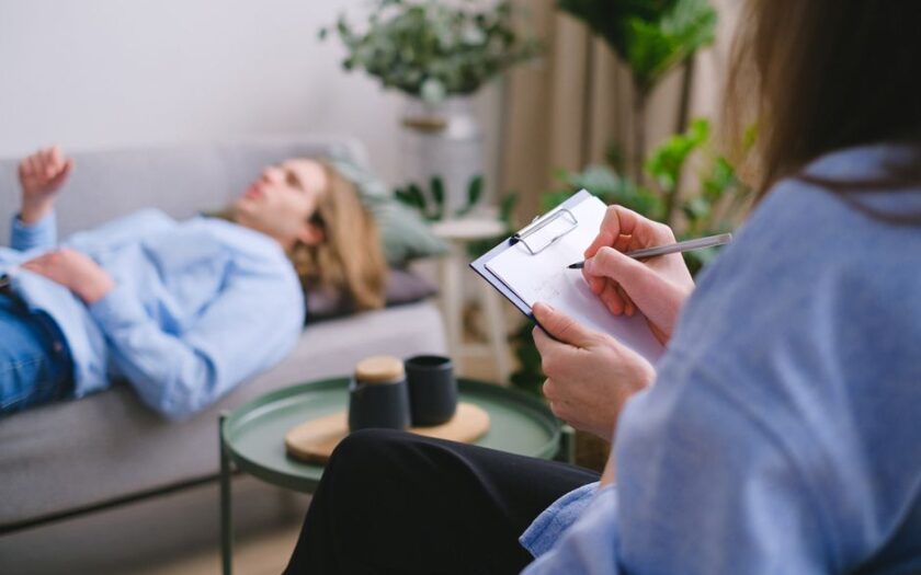 Unrecognizable professional therapist writing on clipboard while sitting against male client lying on couch on blurred background during mental health therapy - Photo by SHVETS production on Pexels