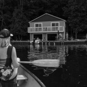 Woman paddling a canoe towards a lakeside house, capturing summer relaxation. - Photo by Paige Thompson on Pexels