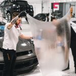 Two professionals applying protective film to a luxury car in a modern garage. - Photo by WAVYVISUALS on Pexels