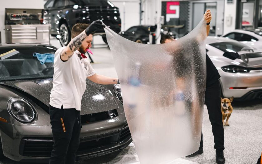 Two professionals applying protective film to a luxury car in a modern garage. - Photo by WAVYVISUALS on Pexels